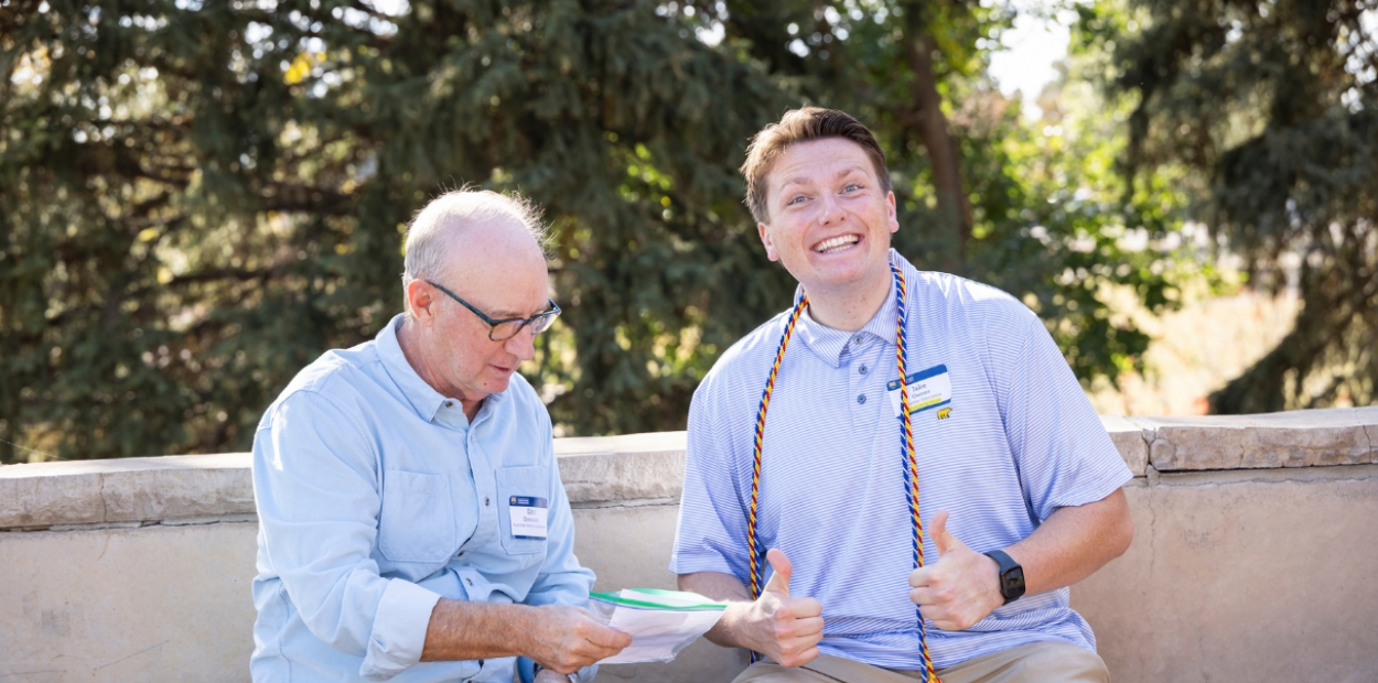 An elderly man and a younger man sitting on a bench, laughing together.