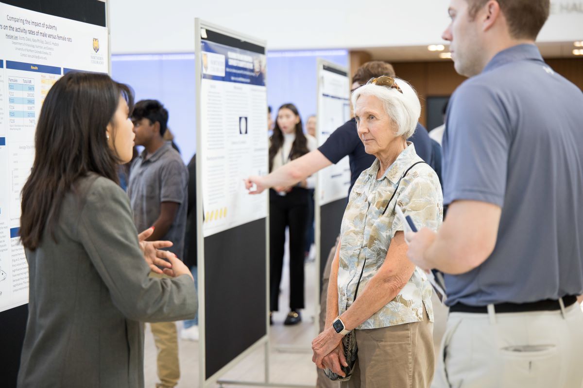 two people talk with a student in front of a research poster