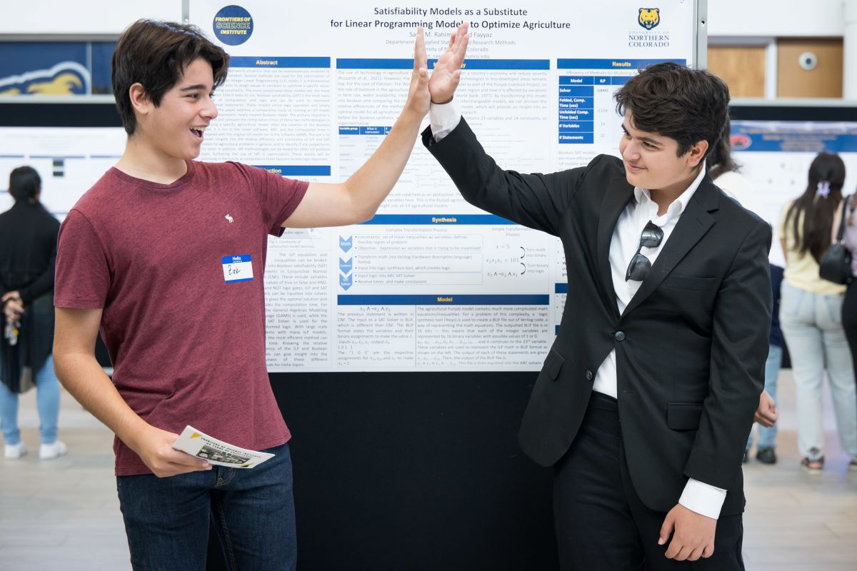 two students high five in front of a research poster