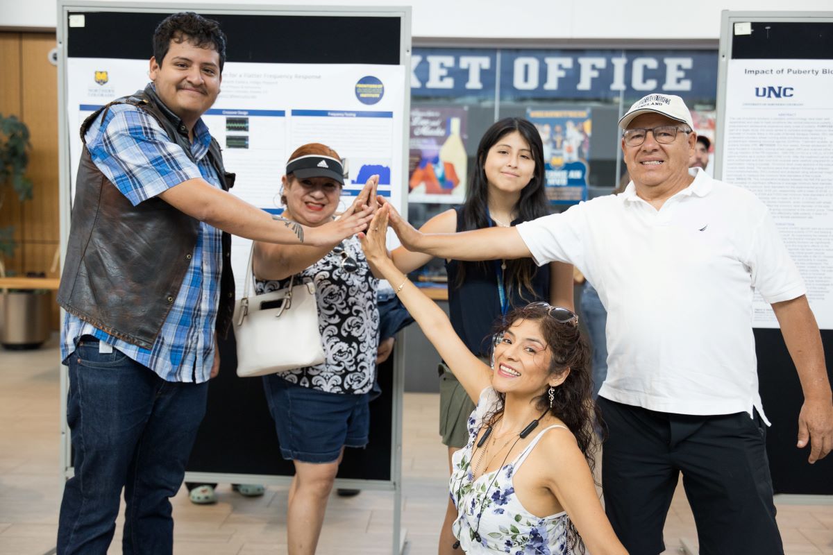 five students high five in front of a research poster