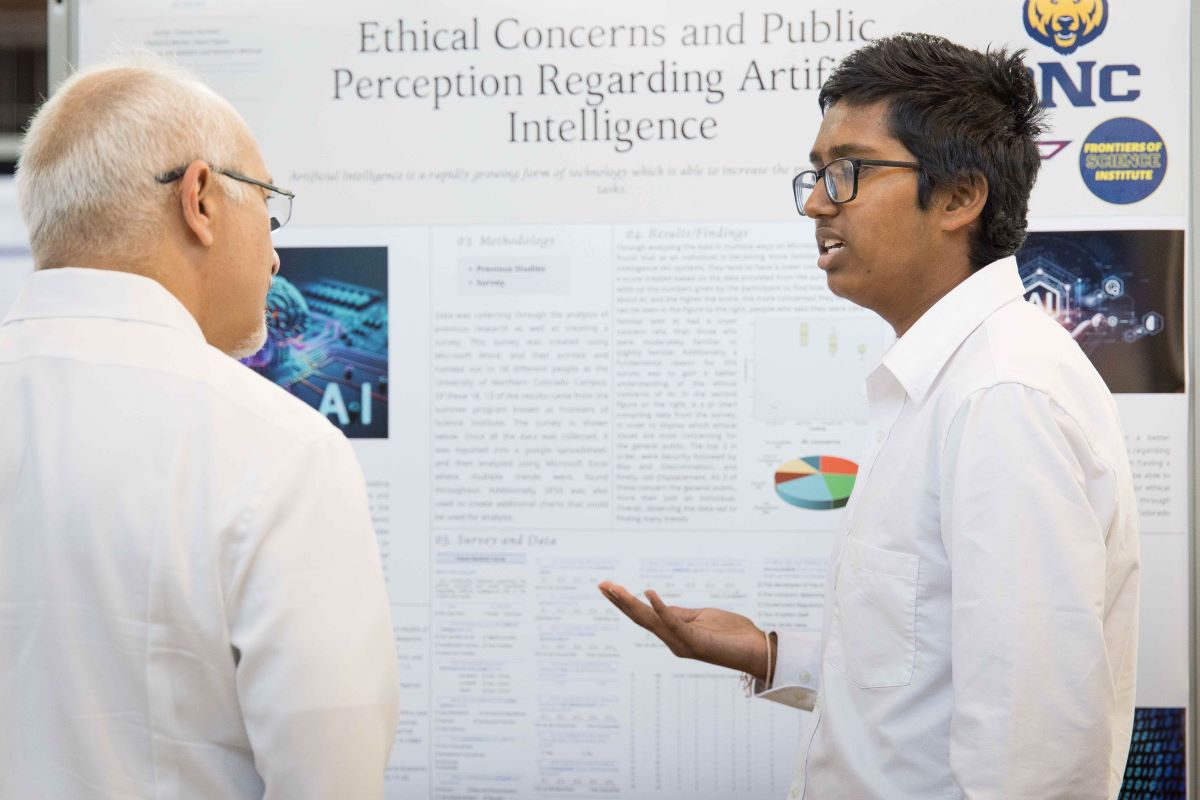 a student speaks with Dean Kamel Hadded in front of a research poster