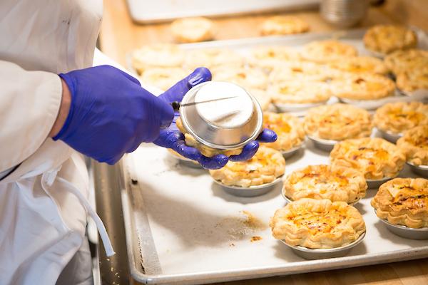 View of pastry chef's hands and pie as they are removed from baking trays.