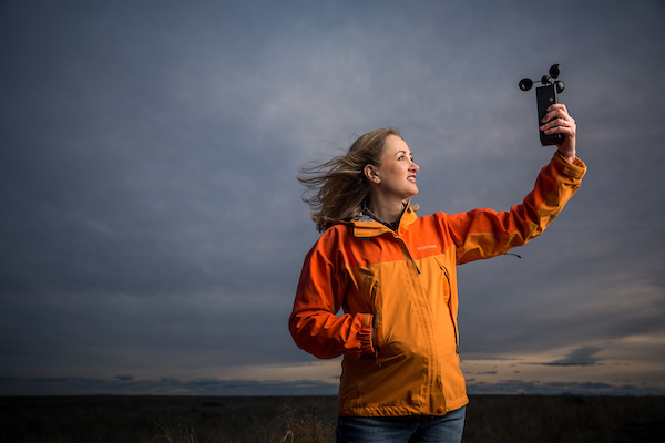 A teacher stands with a camera in a field