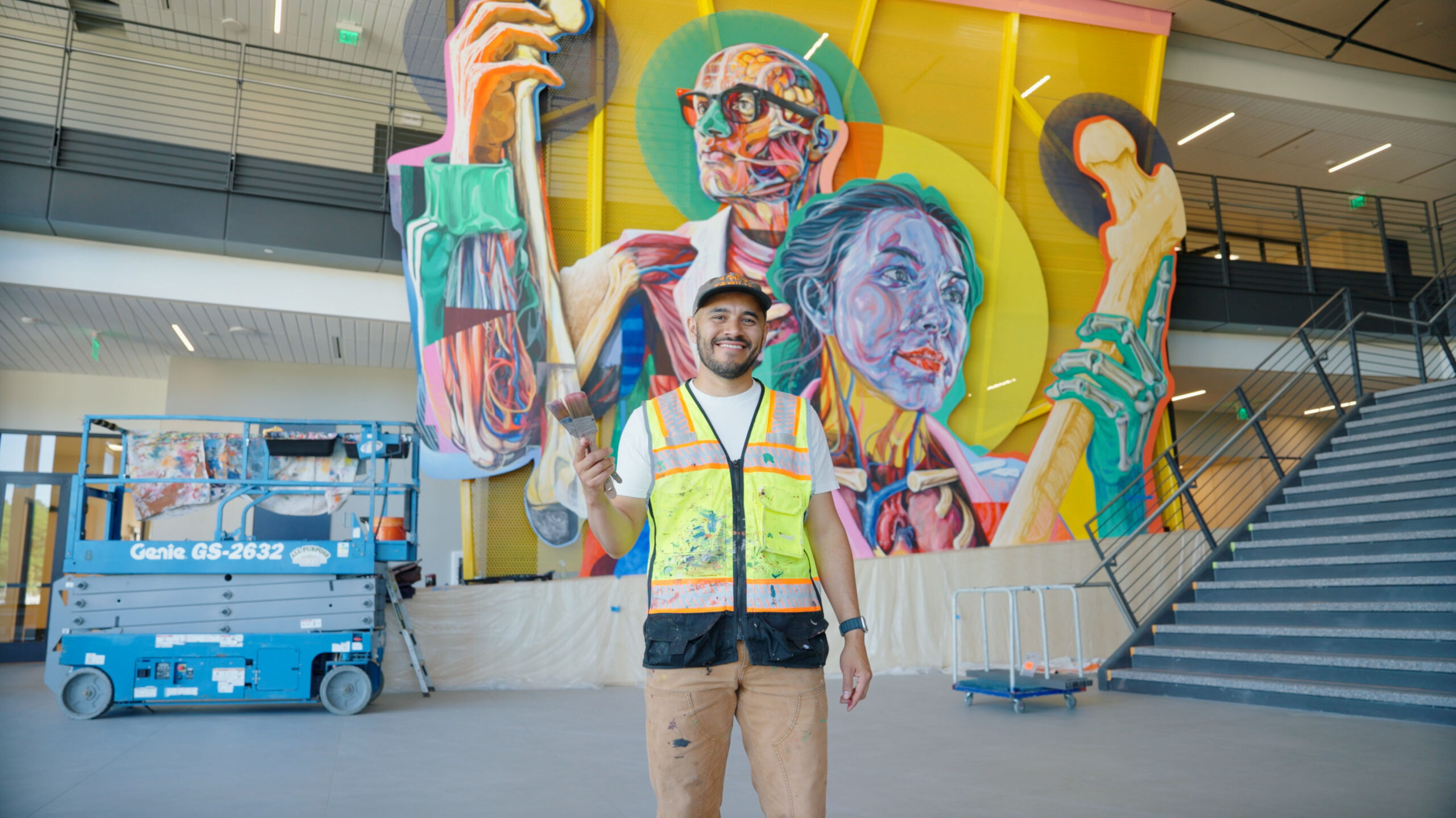 Armando Silva standing in front of his mural smiling and holding a paint brush