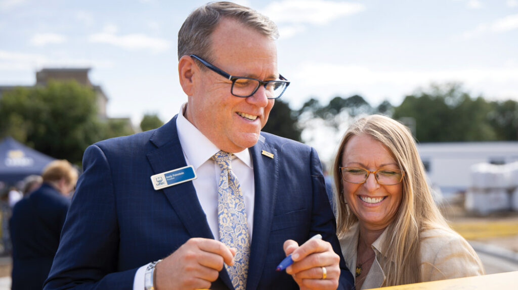 Andy smiling and standing with his wife Keri, signing the final interior beam on the COM.