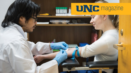 A UNC student in a lab coat drawing blood from a young clinic attendee.