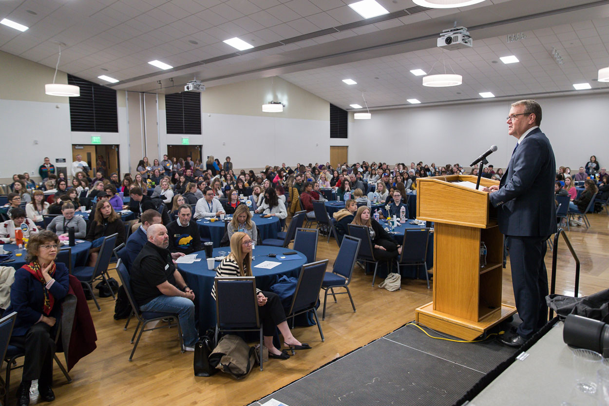 President of UNC, Andy Feinstein, standing at the podium addressing the auditorium.