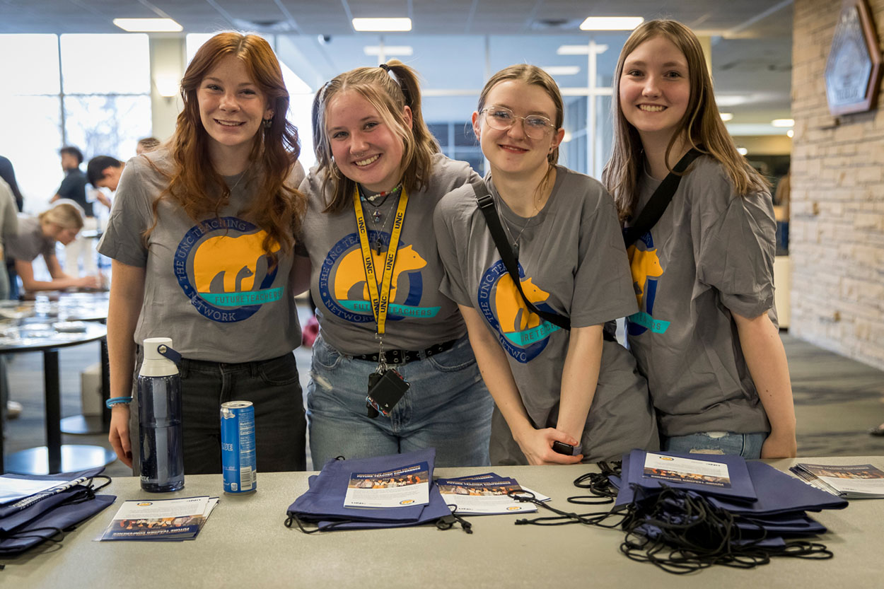 Four student volunteers wearing Future Teacher Conference shirts standing behind a table.