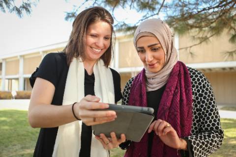Two female presenting individuals looking together at an iPad outside of Michener library.