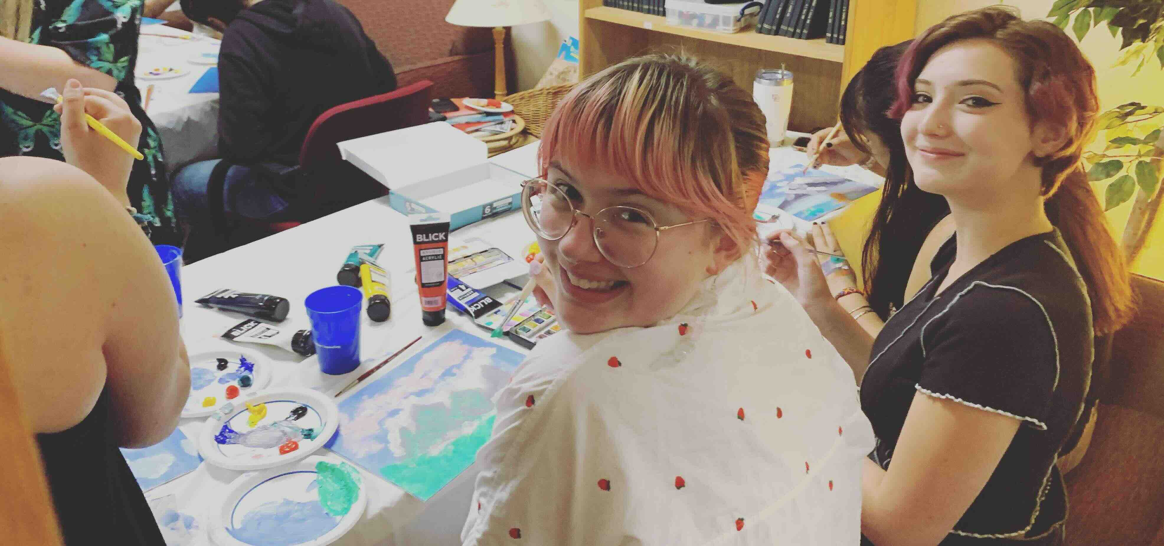 Image of students painting on canvases and smiling at camera