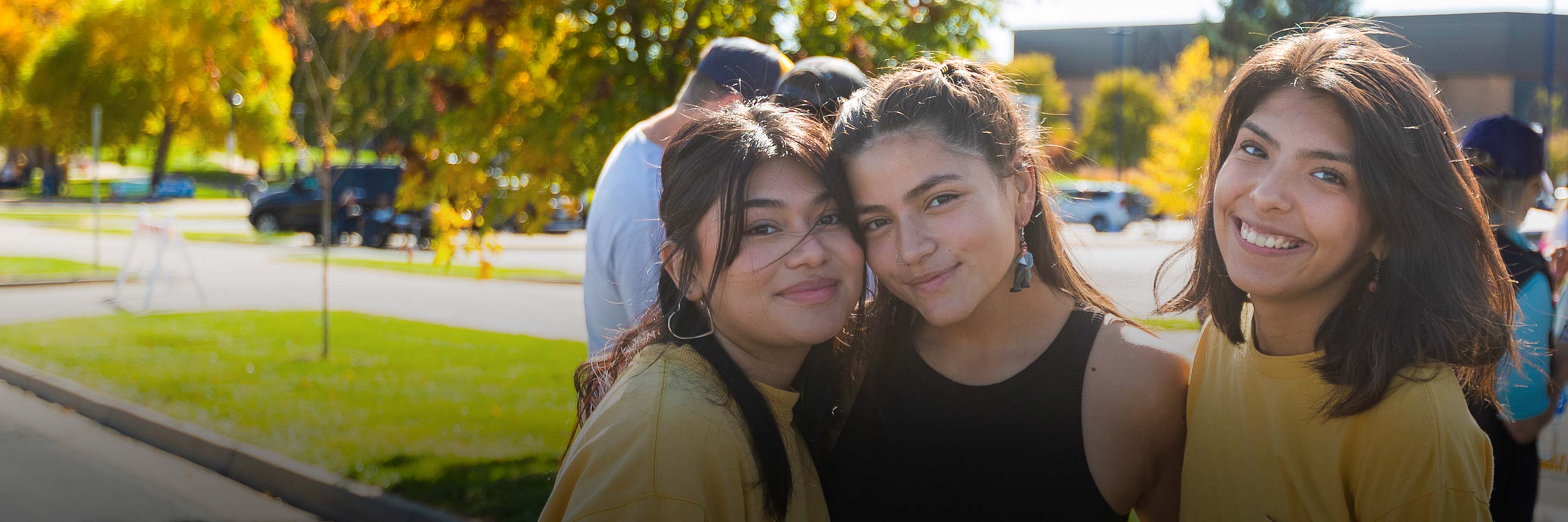 Three college students smiling and standing together outside during an event to celebrate Hispanic/Latinx communities.