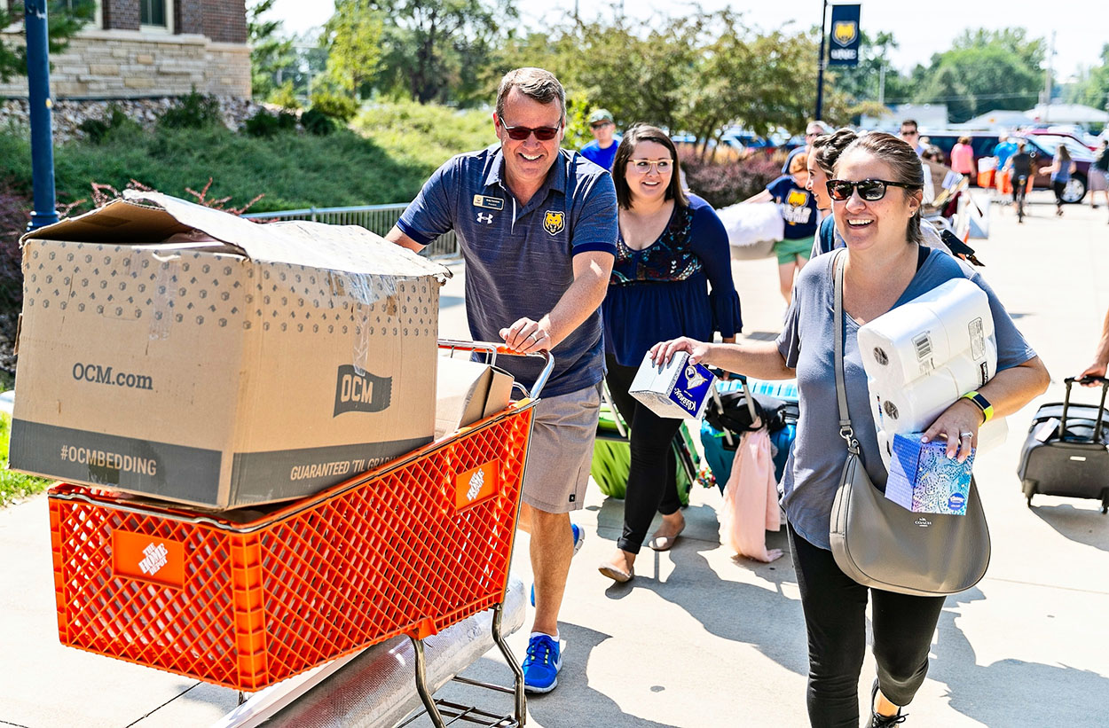 Andy pushes cart of luggage next to students moving into campus.