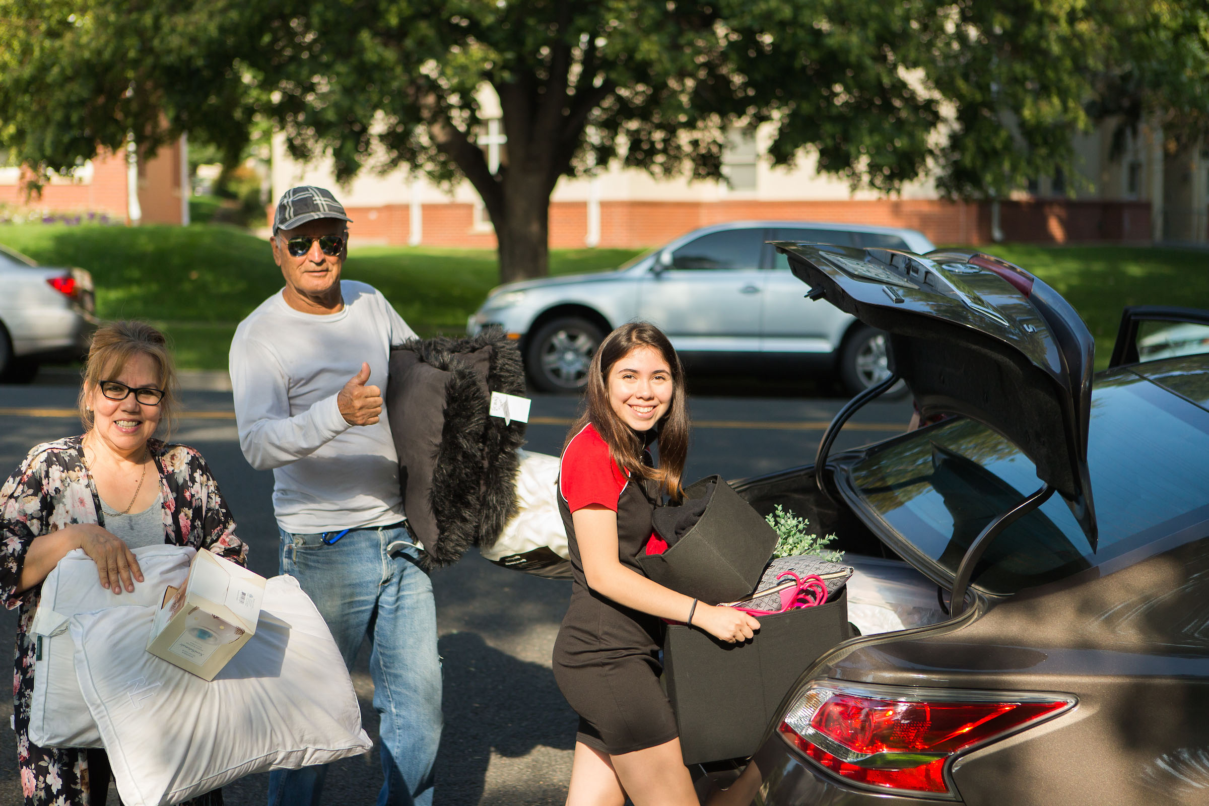 People pose while getting luggage out of the trunk of their car.
