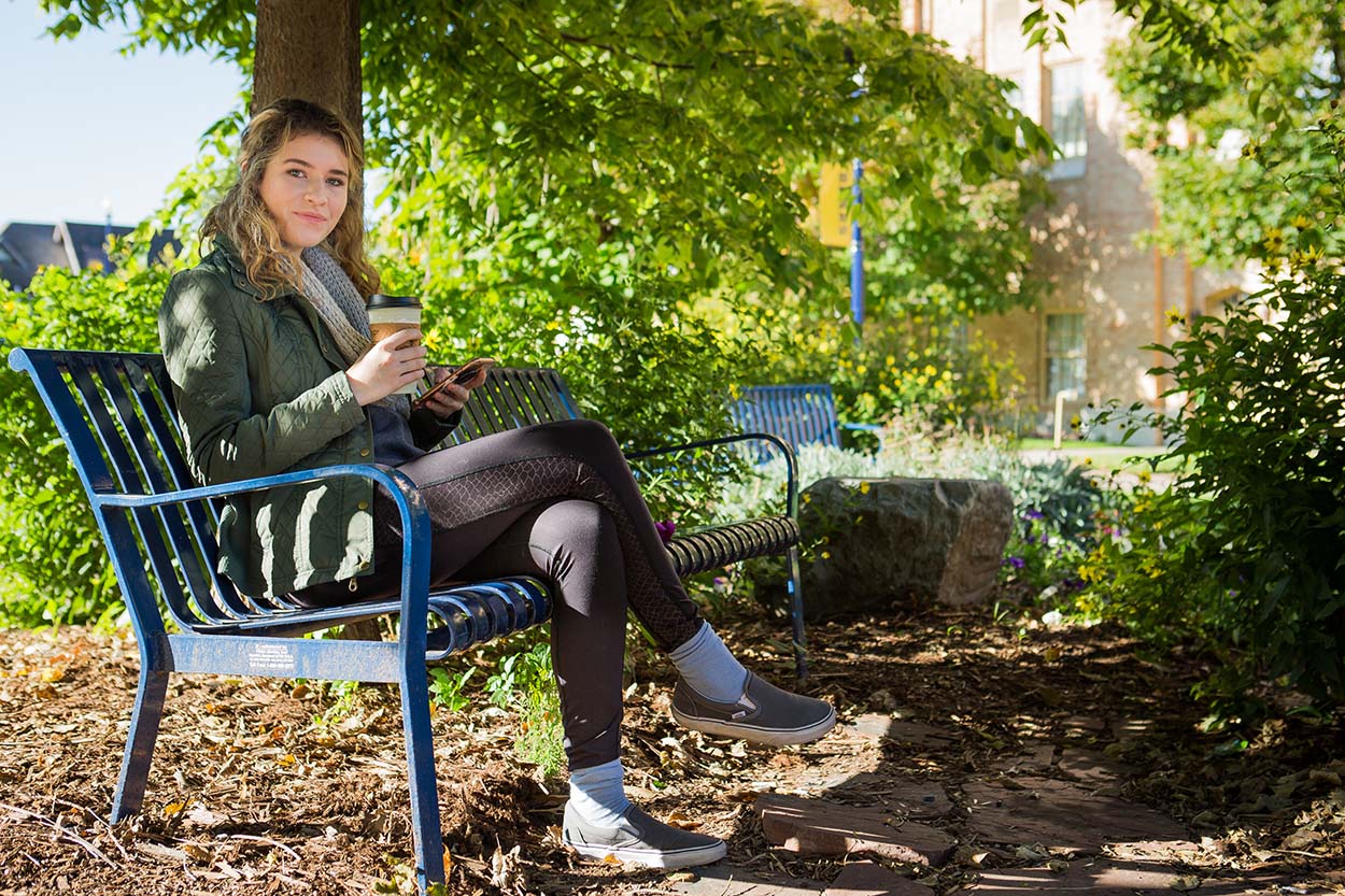 Student sits on a bench drinking coffee.