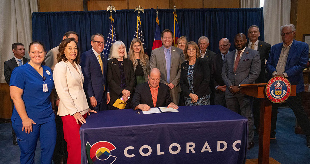 Governor Polis signing HB24-1231 surrounded by supporters of the proposed College of Osteopathic Medicine.