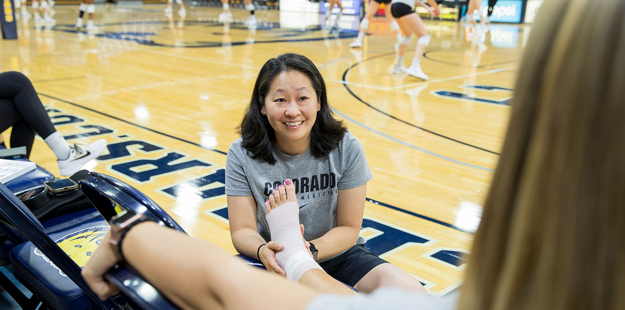 Aimee Miyazawa smiles at a volleyball player after successfully wrapping her injured ankle.