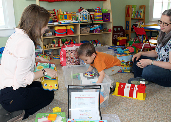 Child reaching into toy bin with two adults around.