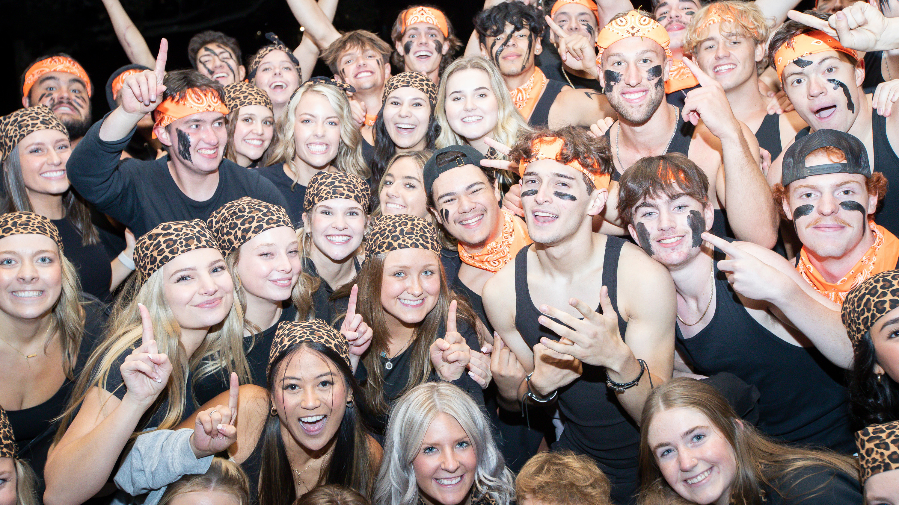 A large number of students wearing black and orange huddled together smiling
