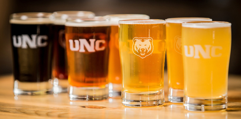 Four beers ranging in colors of brown sitting on a table with a bear logo and UNC on the clear glasses