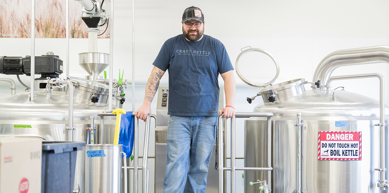 Sean Johnson standing in the brewing laboratory beside steel kettles.