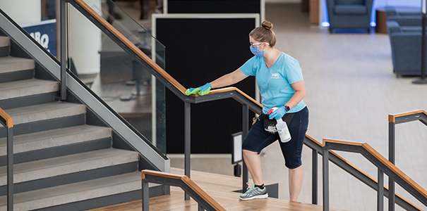 Custodial staff member cleaning handrail in campus commons