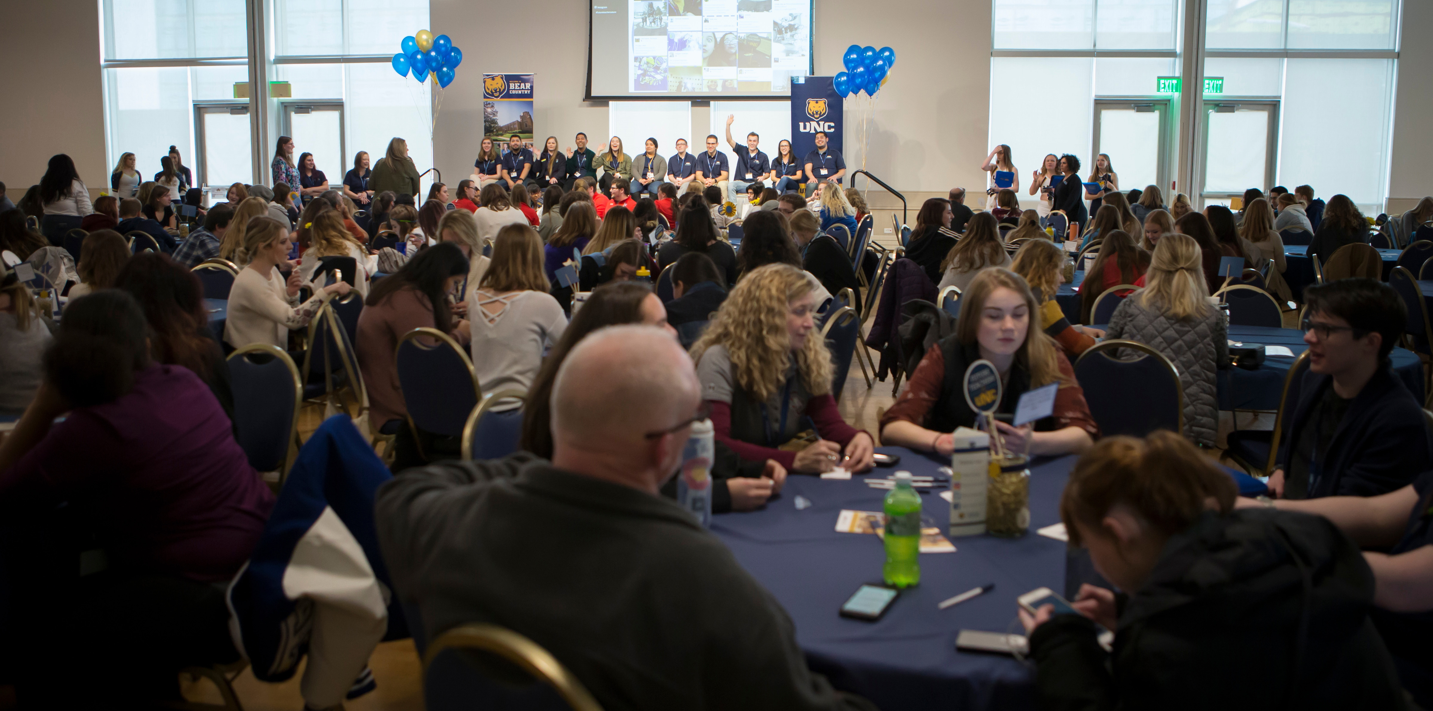 A large room with a crowd of high school students sitting at tables