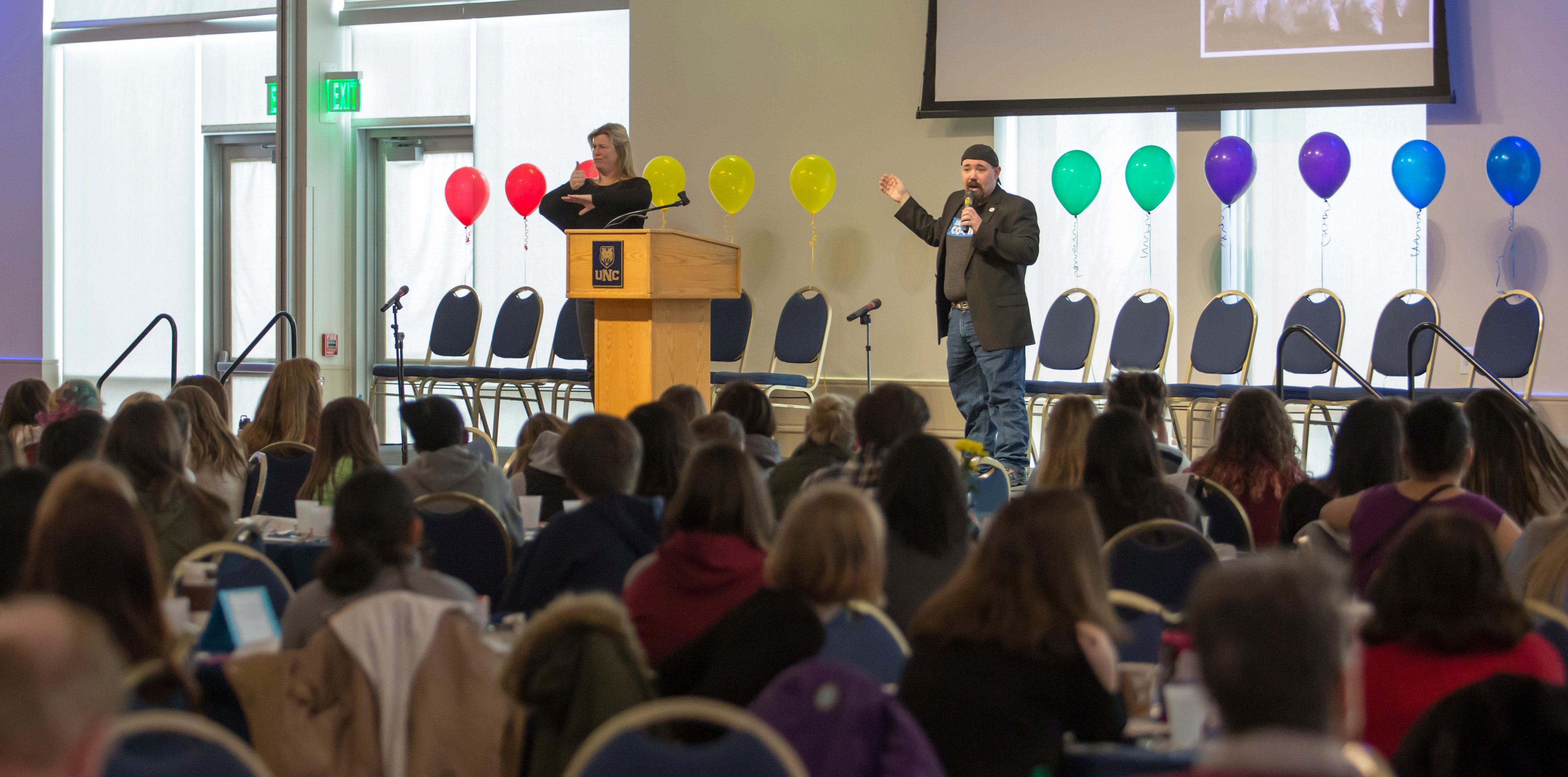 A speaker speaking on a stage to students sitting below