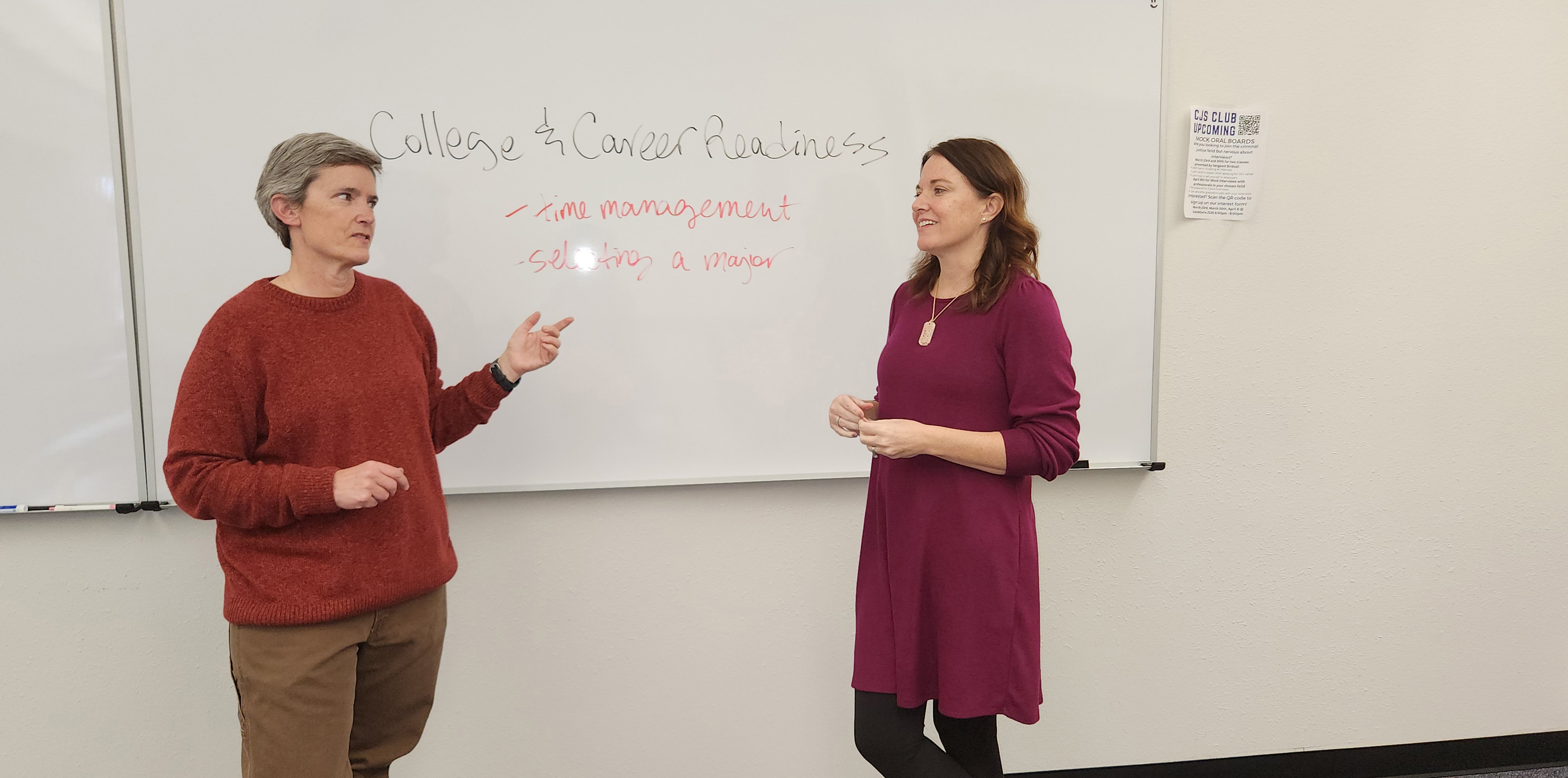 Two woman standing in front of a dry erase board looking at each other while talking
