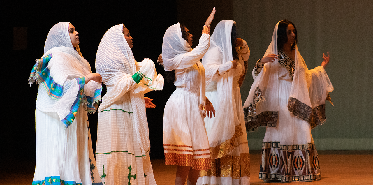 Women wearing white gowns dancing together on a stage