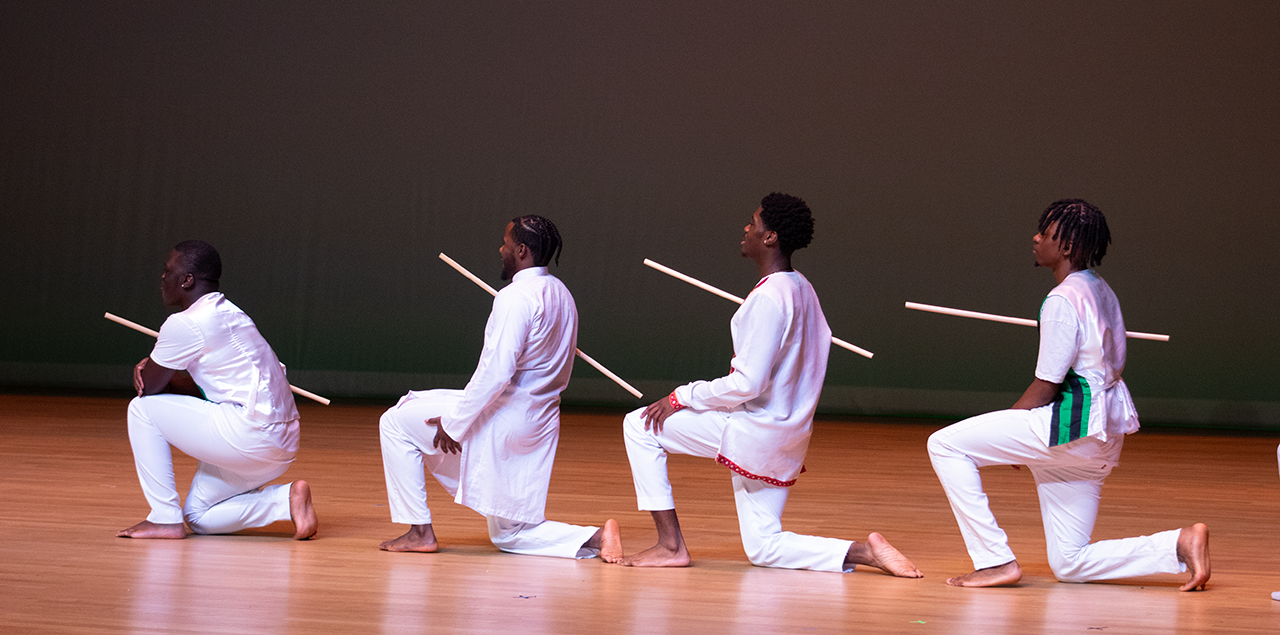 Four men kneeling on their knees in a dance on a stage
