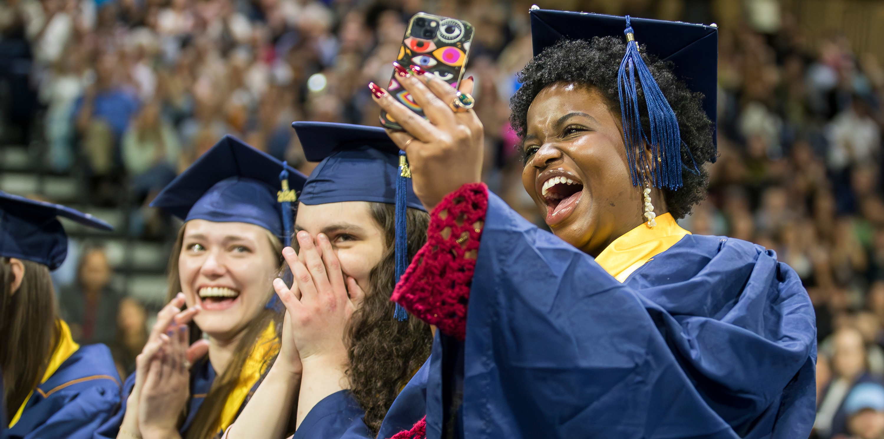 Three graduate students smiling in their cap and gown