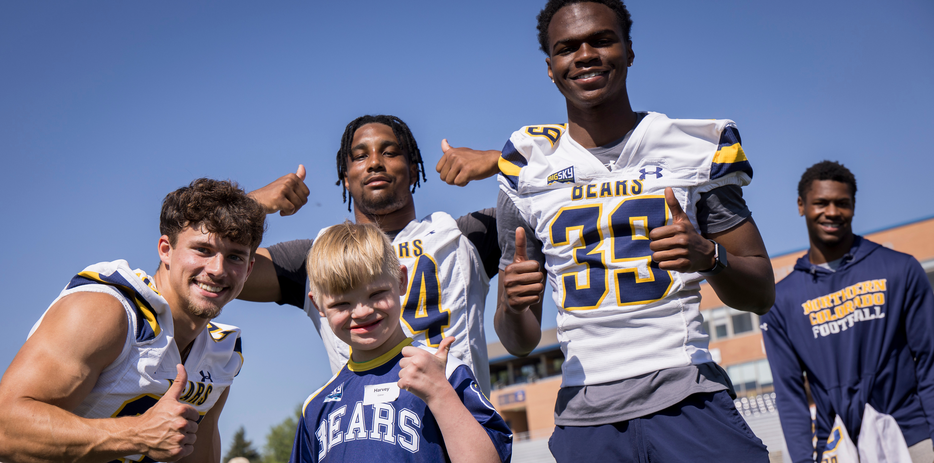 UNC football players posing with a young special needs kid wearing UNC football uniforms