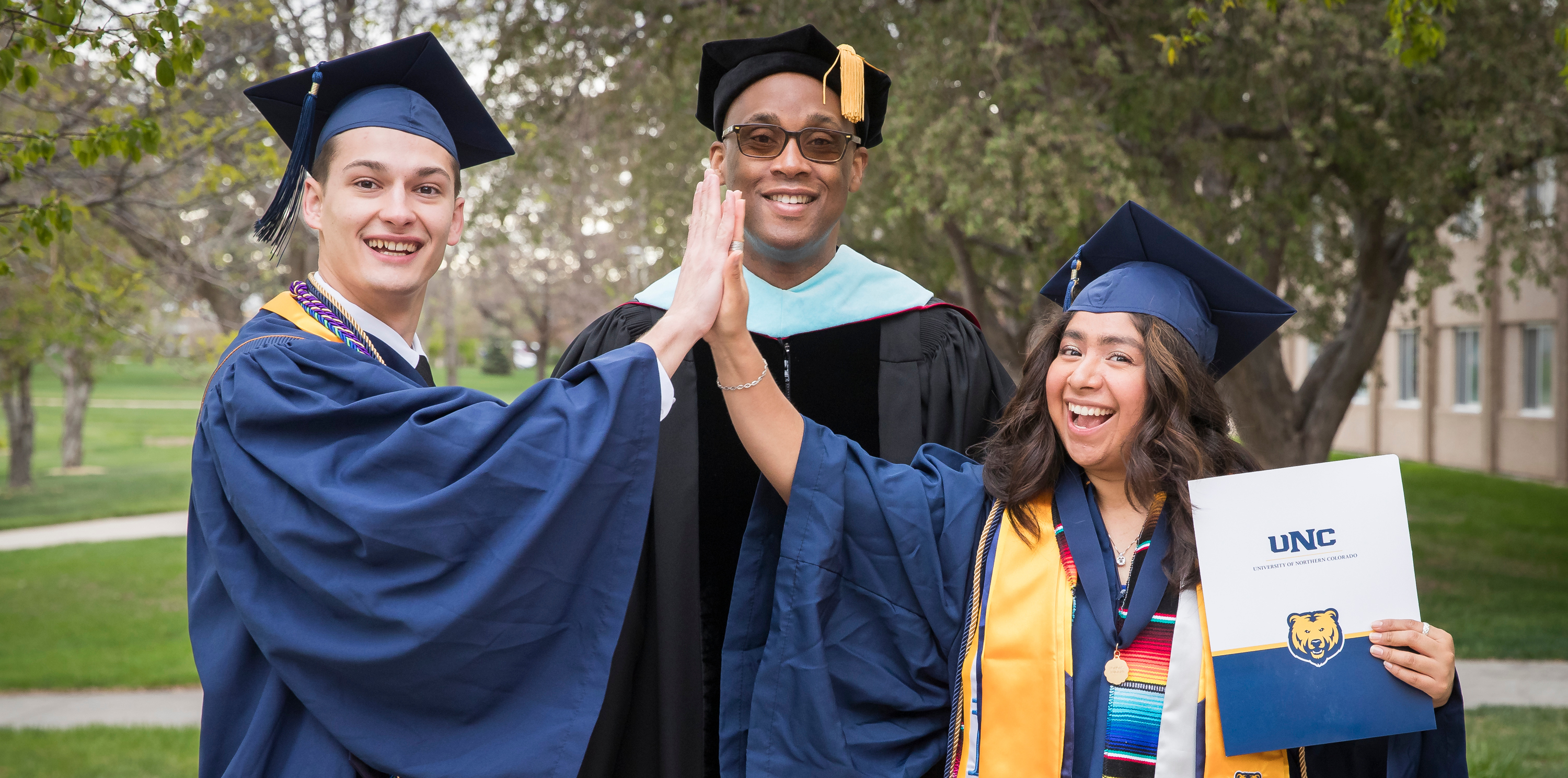 Two students high-fiving in their graduation gowns