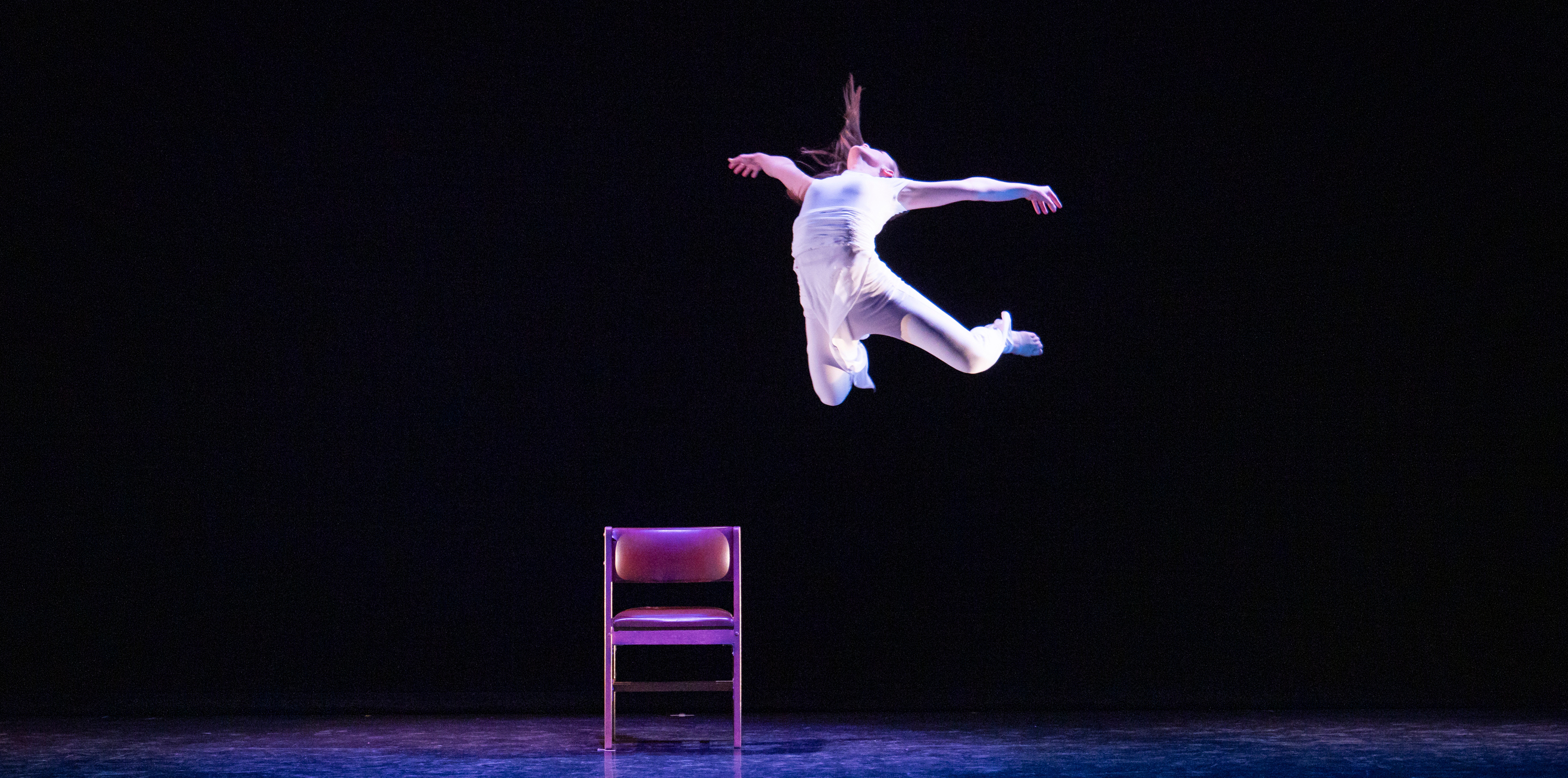 A student dancing leaping into the air above a chair