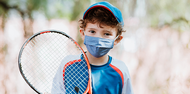 Child with racket and wearing mask